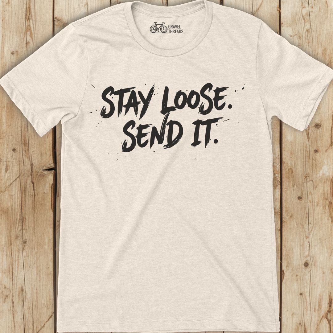 Beige t-shirt with 'Stay Loose. Send It.' text on a wooden surface