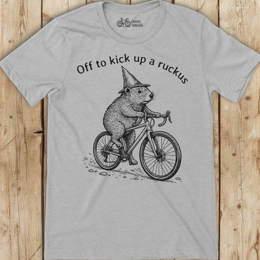 Gray t-shirt with a graphic of a beaver riding a bicycle and text on a wooden surface