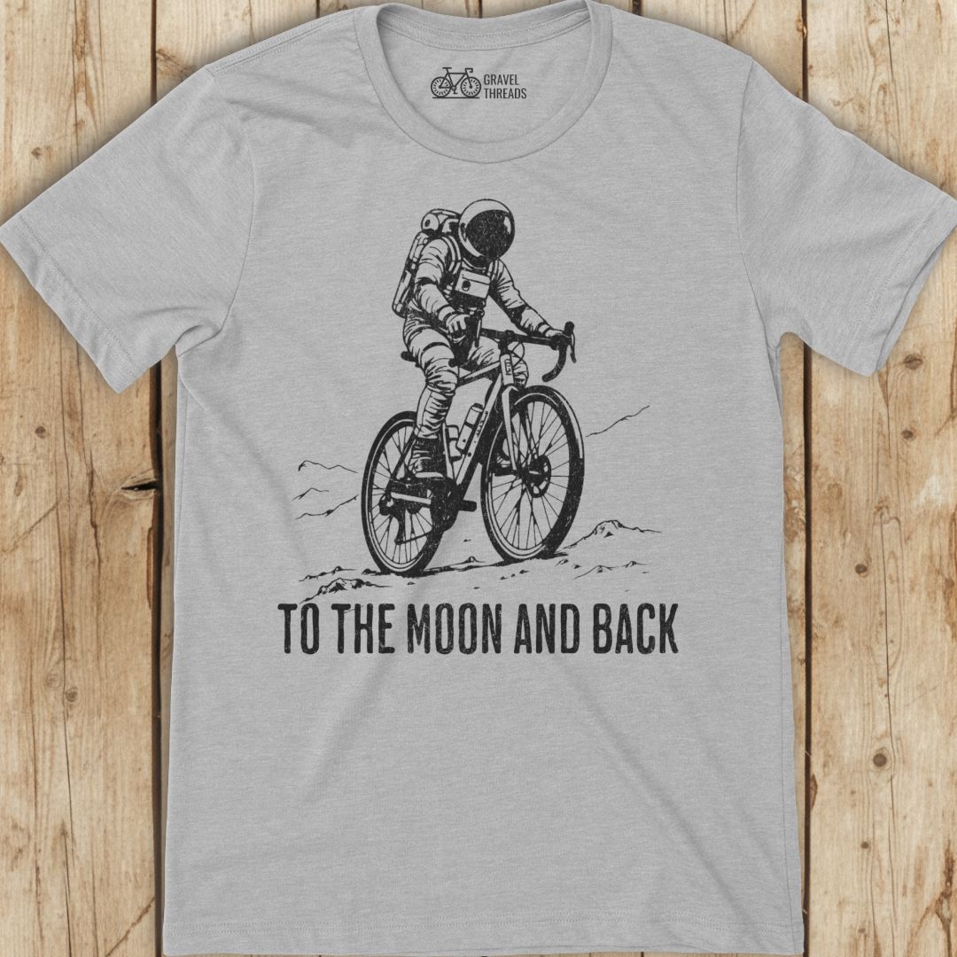 Gray t-shirt with an astronaut riding a bike graphic and 'To the Moon and Back' text on a wooden surface.