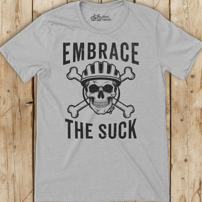 Gray t-shirt with skull and crossbones graphic and text 'Embrace The Suck' on a wooden background