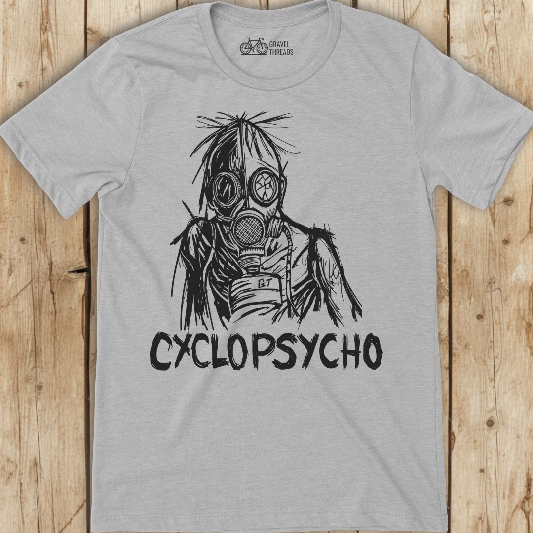 Gray t-shirt with a graphic design of a person wearing a gas mask and the text 'Cyclopsycho' on a wooden surface.