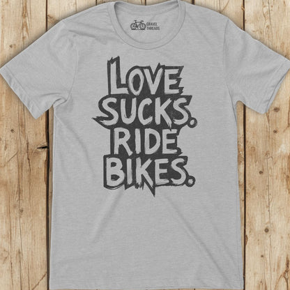 Gray t-shirt with 'I Love Sucks. Ride Bikes.' text on a wooden surface