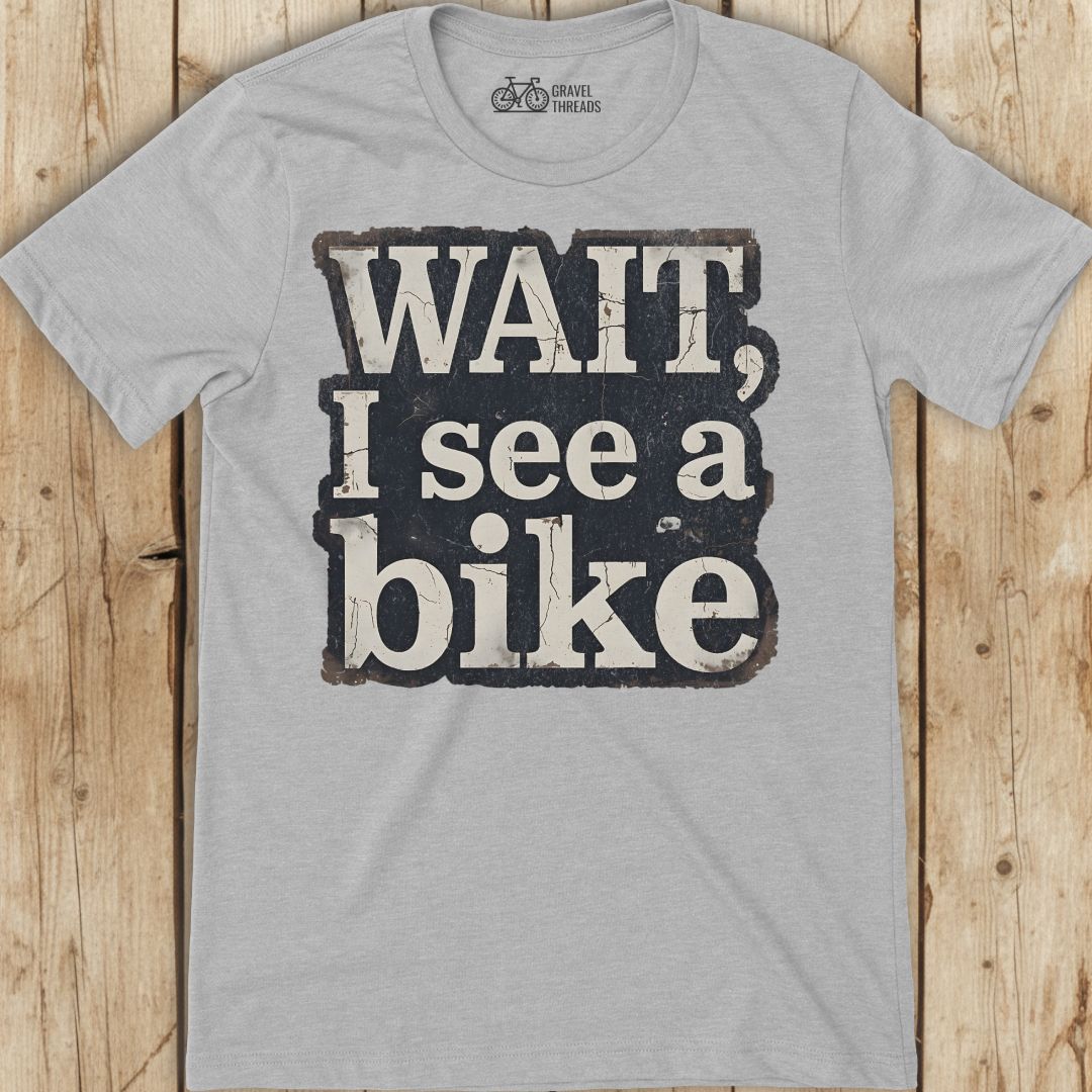 Gray t-shirt with 'Wait, I see a bike' text on a wooden surface