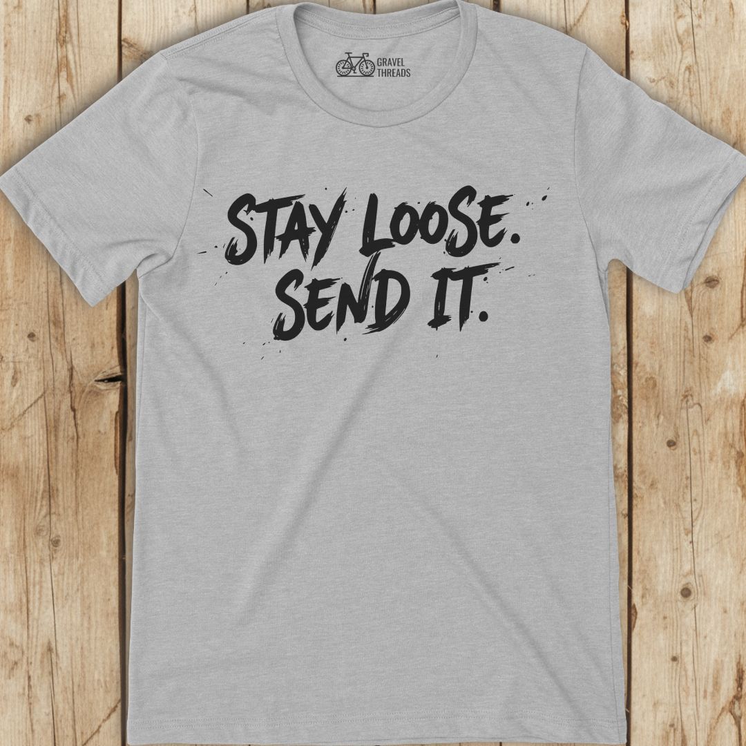 Gray t-shirt with 'Stay Loose. Send It.' text on a wooden surface