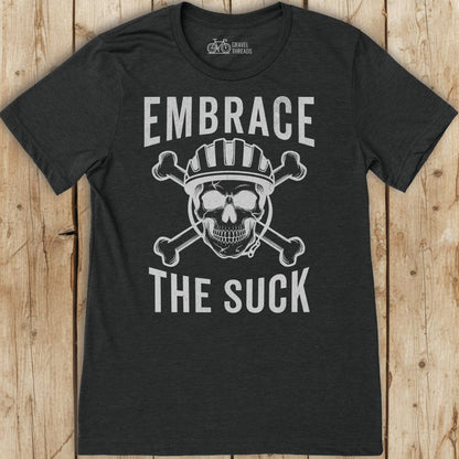 Black t-shirt with skull and crossbones design and text 'Embrace The Suck' on a wooden background