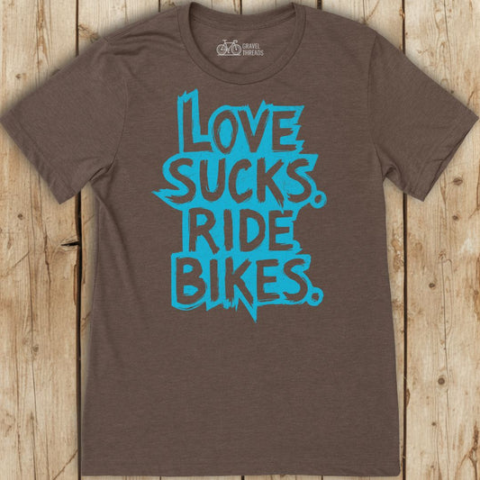Brown t-shirt with blue text 'Love sucks. Ride bikes.' on a wooden surface