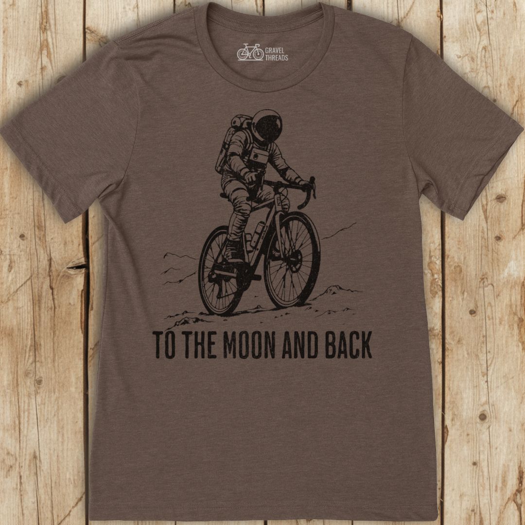 Brown t-shirt with an astronaut on a bike graphic and 'To the Moon and Back' text on a wooden surface.