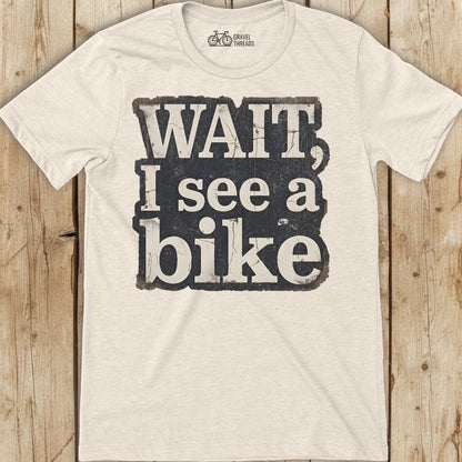Off white t-shirt with 'Wait, I see a bike' text on a wooden surface