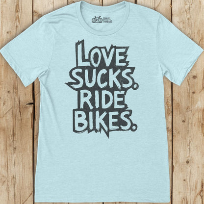 Light blue t-shirt with 'I Love Sucks. Ride Bikes.' text on a wooden surface