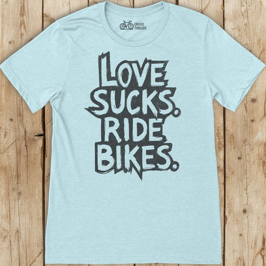 Light blue t-shirt with 'I Love Sucks. Ride Bikes.' text on a wooden surface