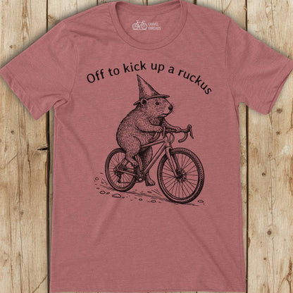 Red t-shirt with a graphic of a beaver on a bicycle and text 'Off to kick up a ruckus' on a wooden surface.