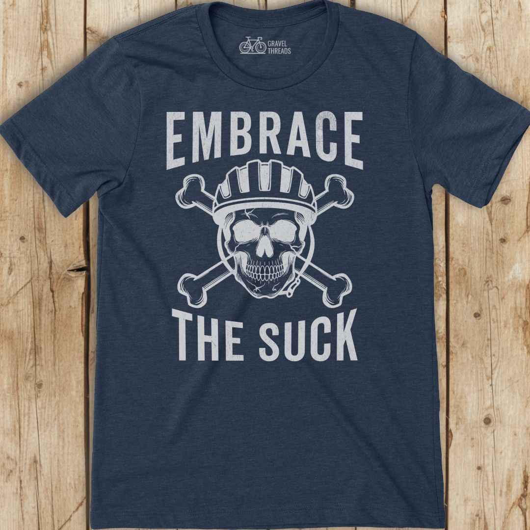 Navy blue t-shirt with skull graphic and text 'Embrace The Suck' on a wooden surface
