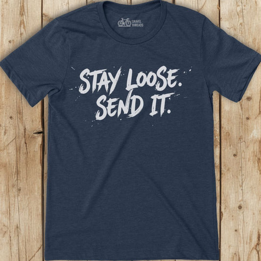 Navy blue t-shirt with white text 'Stay Loose. Send It.' on a wooden surface