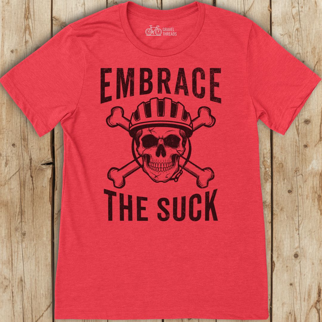 Red t-shirt with skull and crossbones graphic and text 'Embrace The Suck' on a wooden background