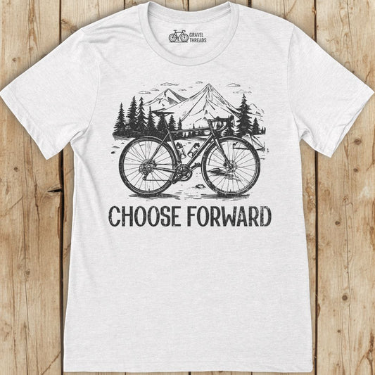 White t-shirt with a bicycle graphic and 'Choose Forward' text on a wooden surface